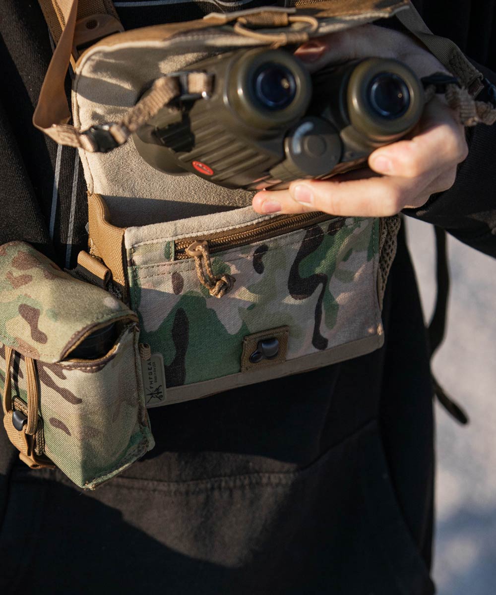 Multicam binocular chest harness with coyote trim and a side pouch, holding green binoculars.