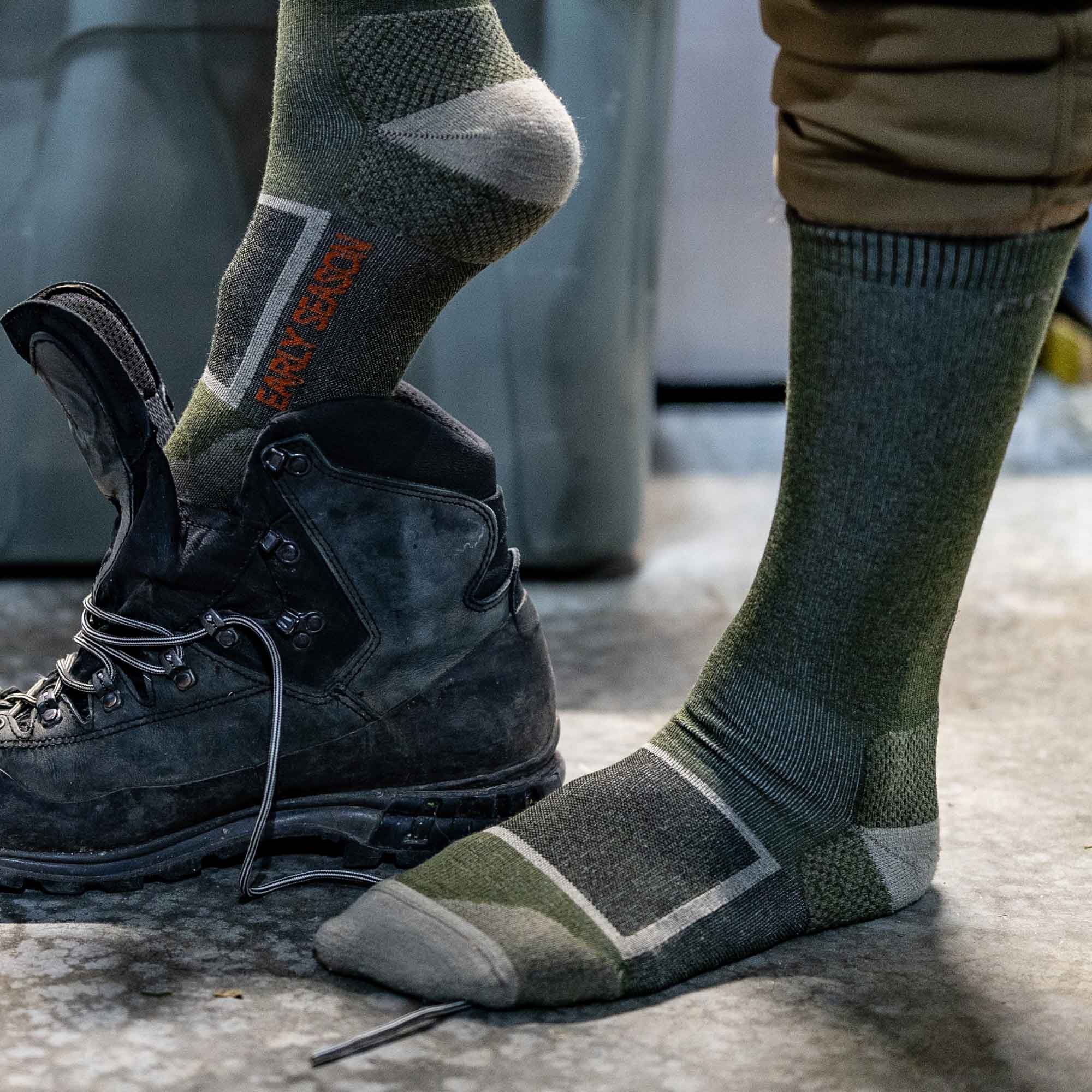 Olive green and grey patterned socks, one worn and one being removed from a black hiking boot, display "EARLY SEASON" text and distinct knit textures.
