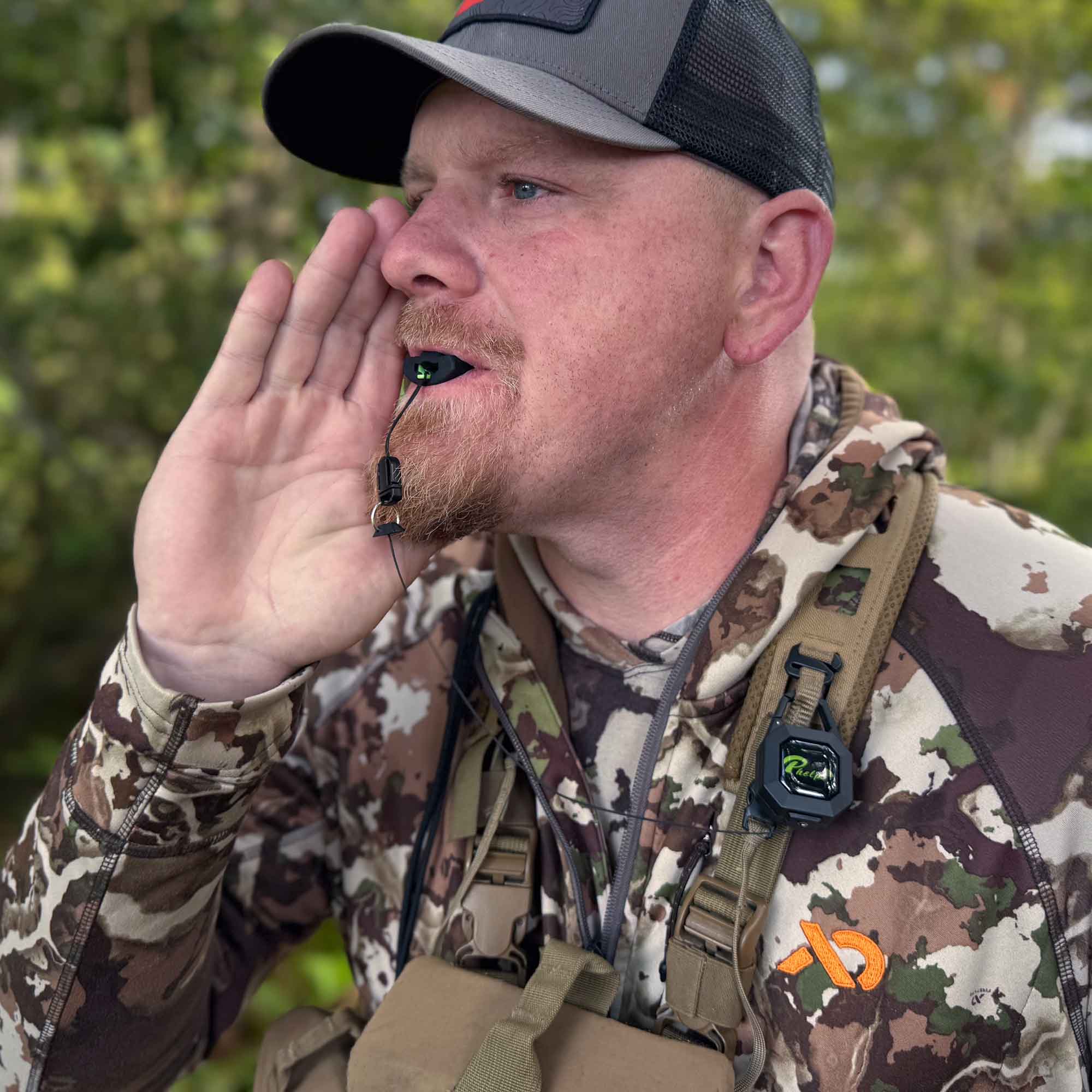 Hunter using black-green Phelps elk call with clip-on holder on camo jacket.