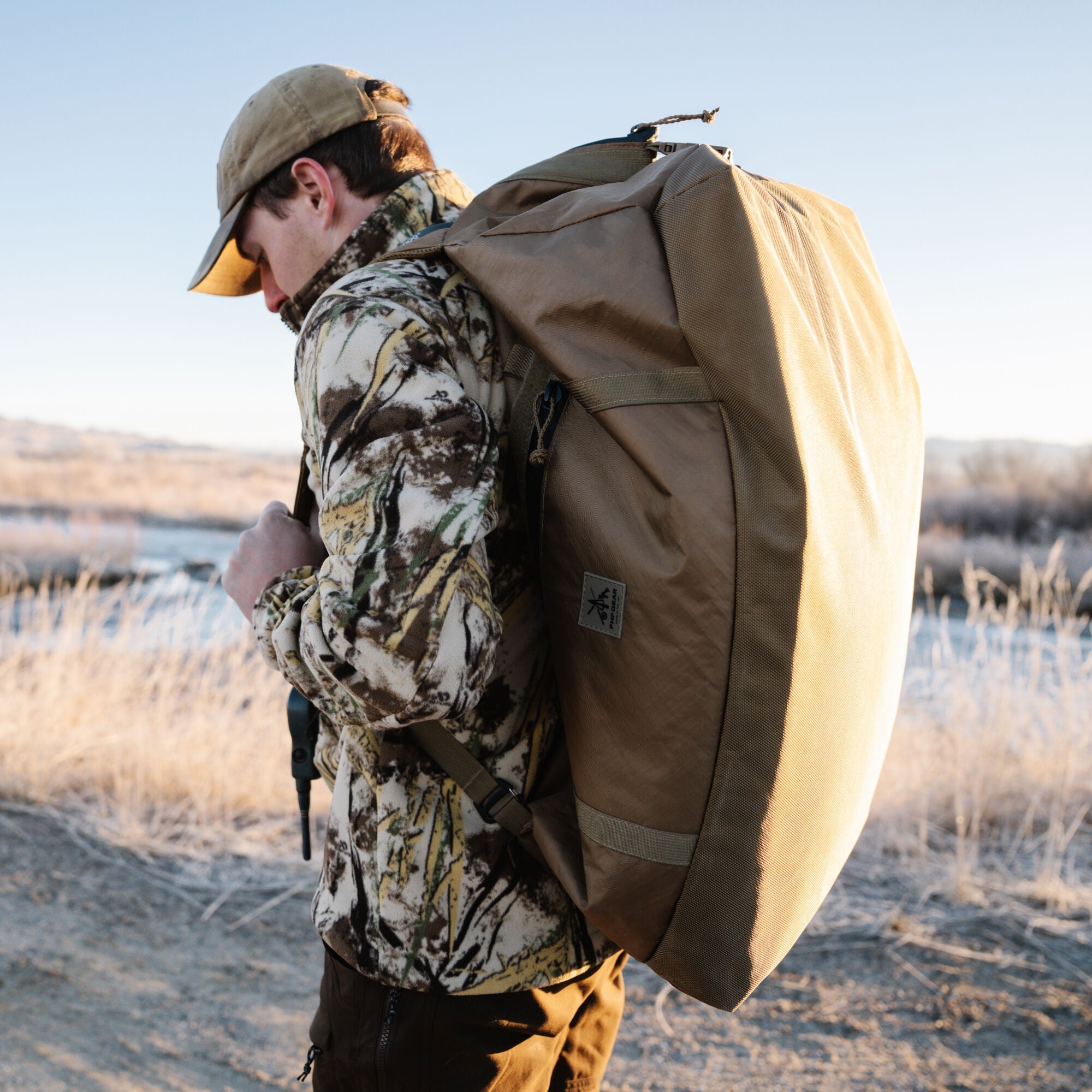 Large coyote pack with logo patch on man's back in frosty landscape.