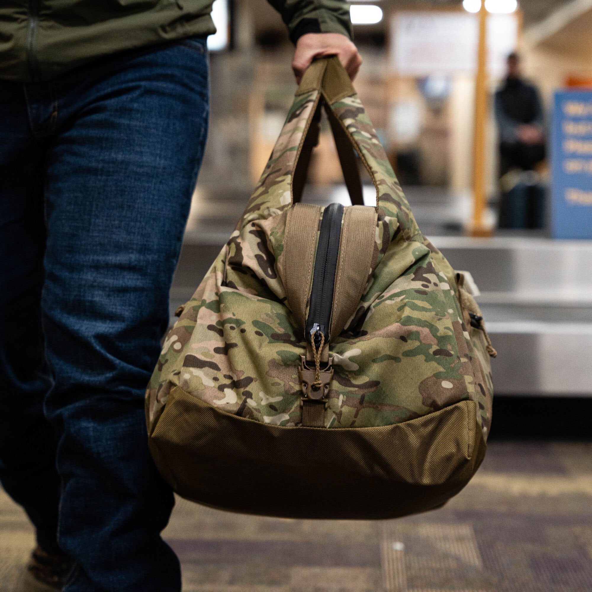 Multicam camouflage duffel bag with olive base and central black zipper held by person.