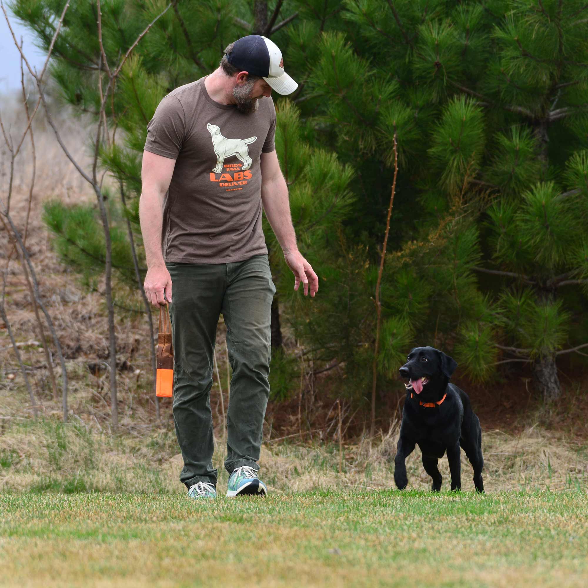 Trainer with black lab throwing bumper.