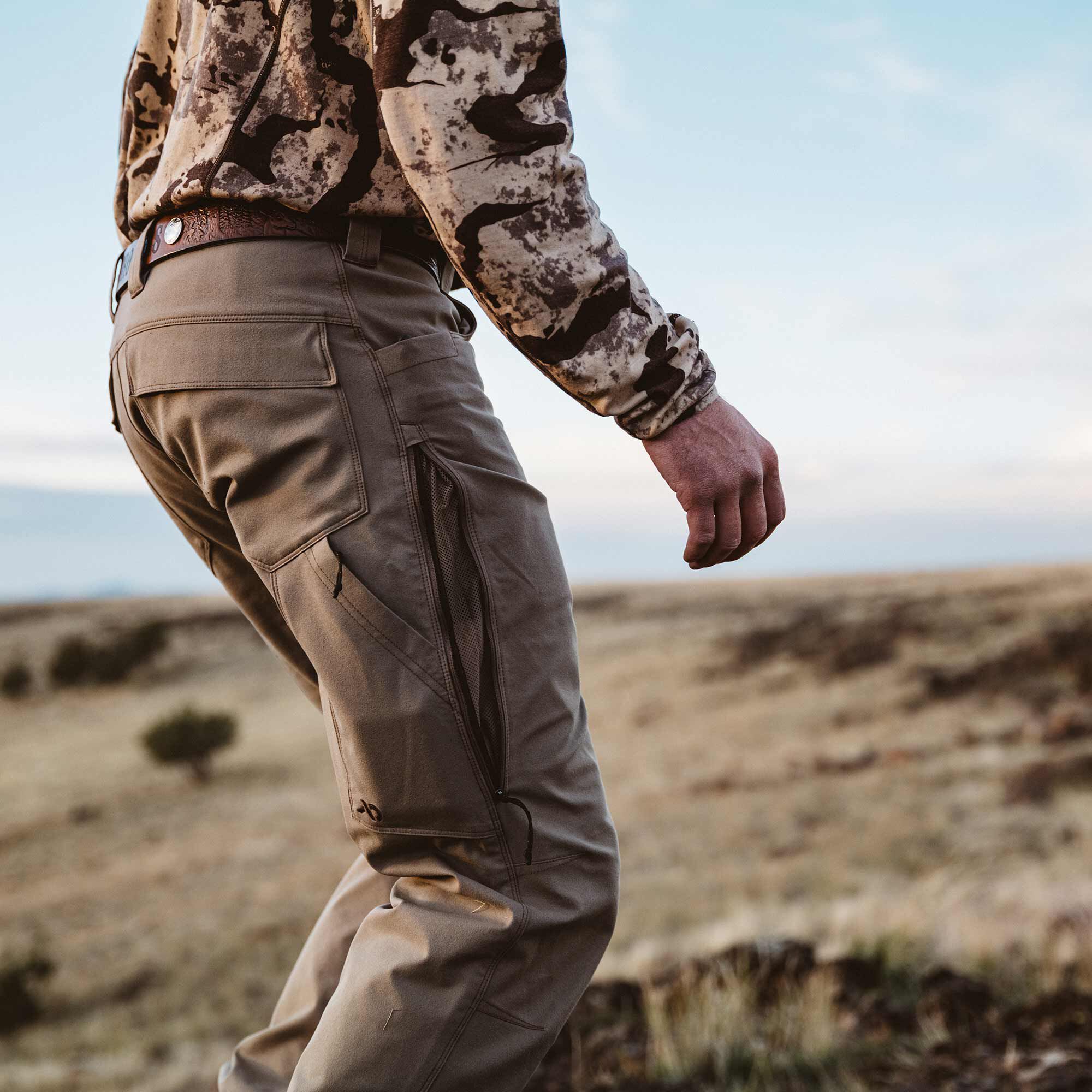 Tan hiking pants featuring rear flap pockets and zippered side cargo pockets, one open to reveal mesh lining.