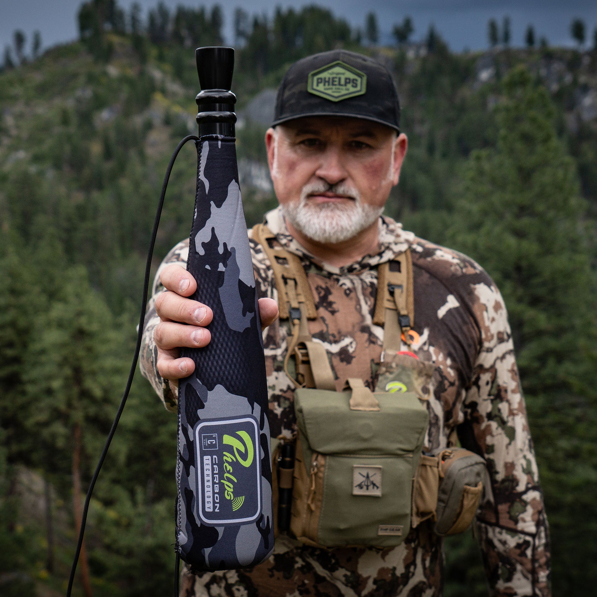Black and gray camo Phelps elk call with mouthpiece, held by hunter.
