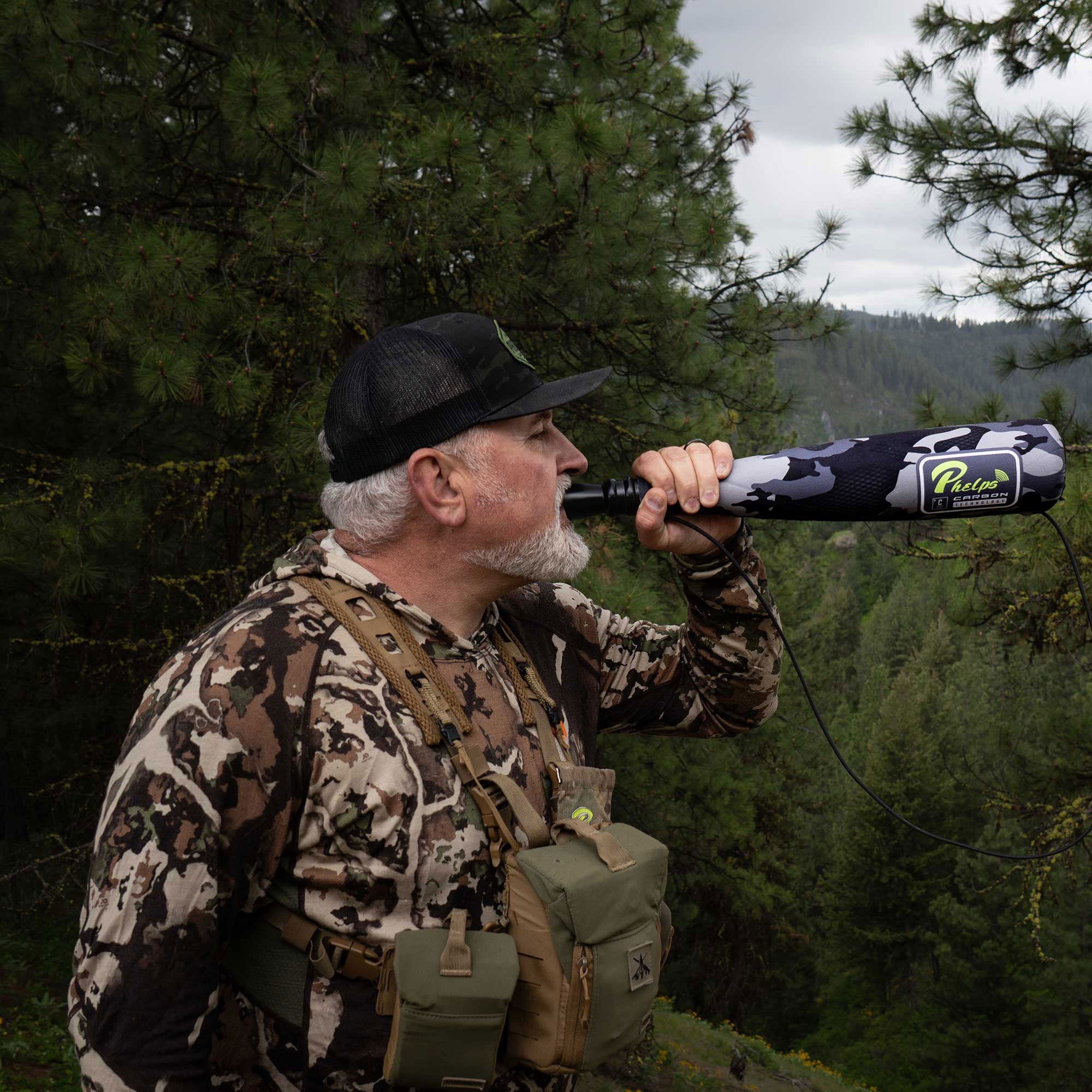 Man blowing into a grey camo Phelps Carbon Technology elk call outdoors.