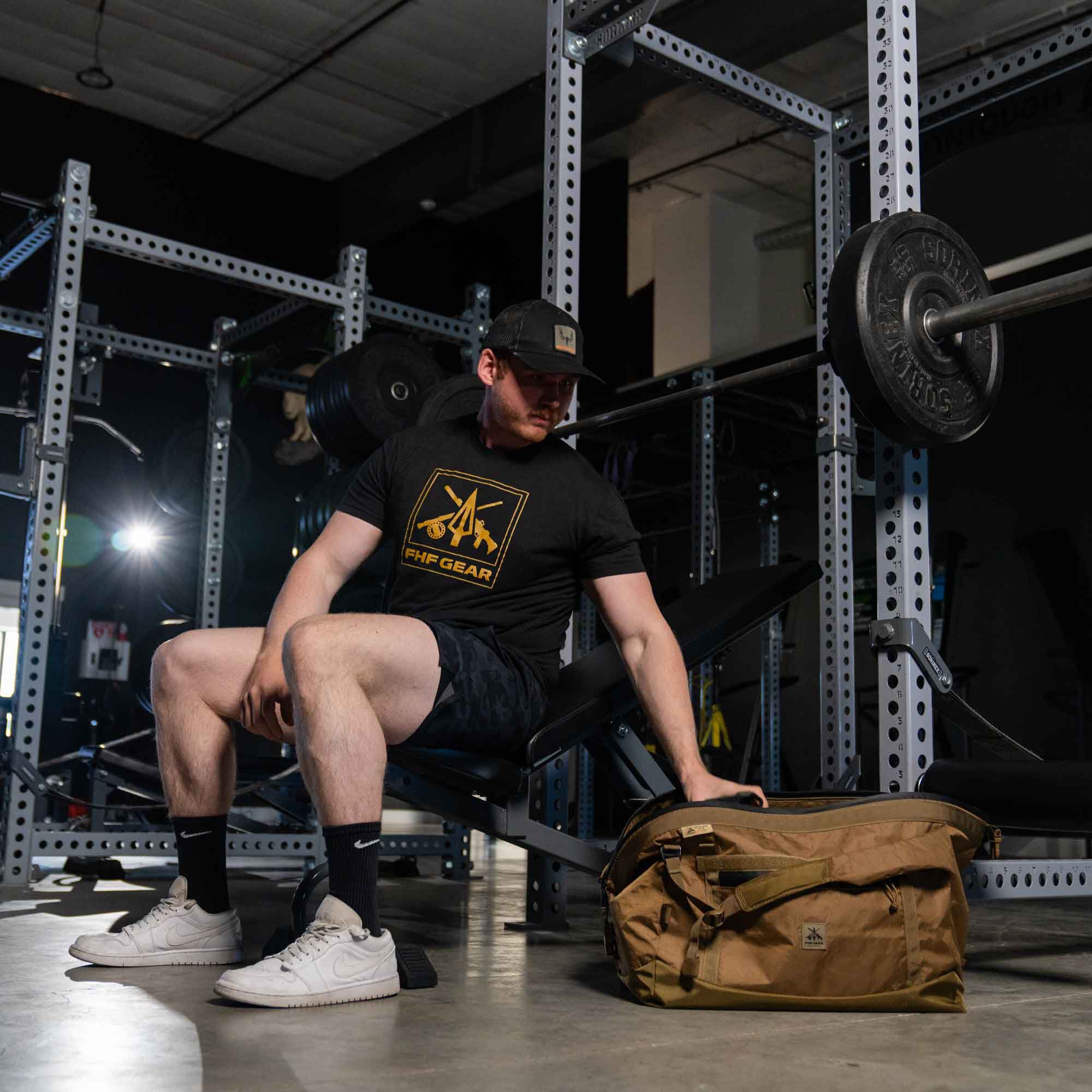 Tan duffel bag with logo, next to man sitting on weight bench.