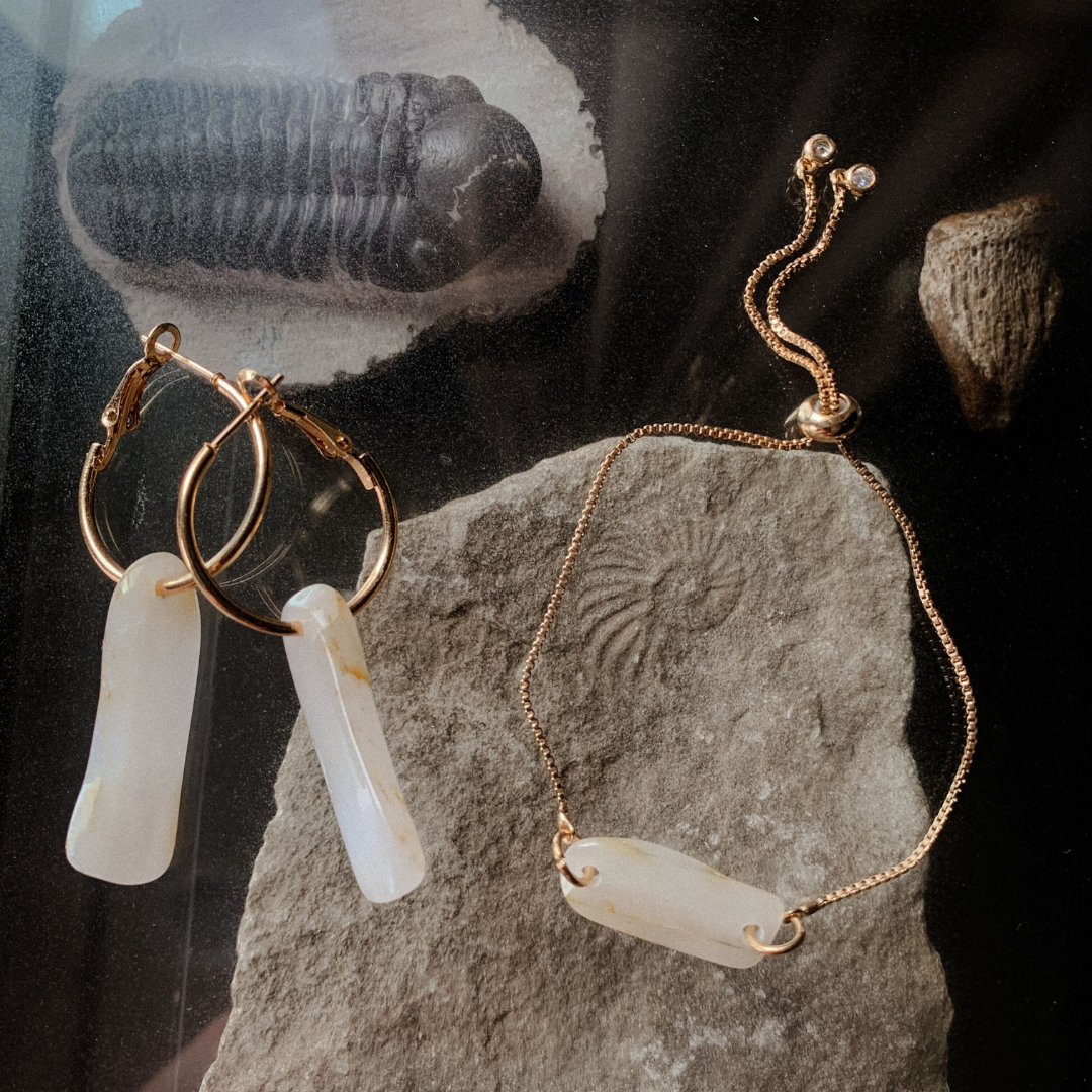 Gold-toned hoop earrings and adjustable bracelet with pale rectangular stones on a rock.