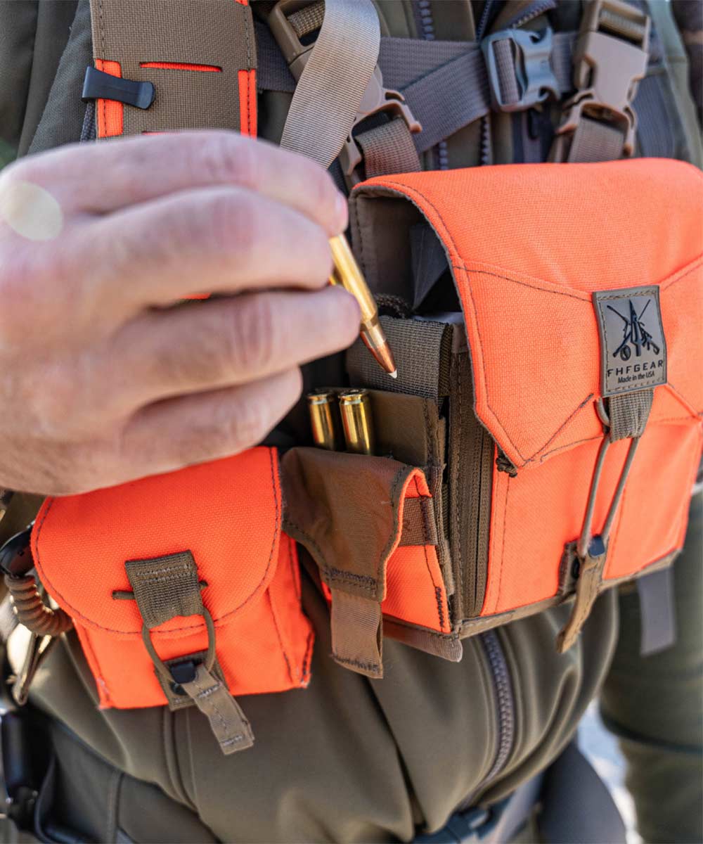 Orange FHFGEAR bino harness with ammo loops, hand inserting cartridge.