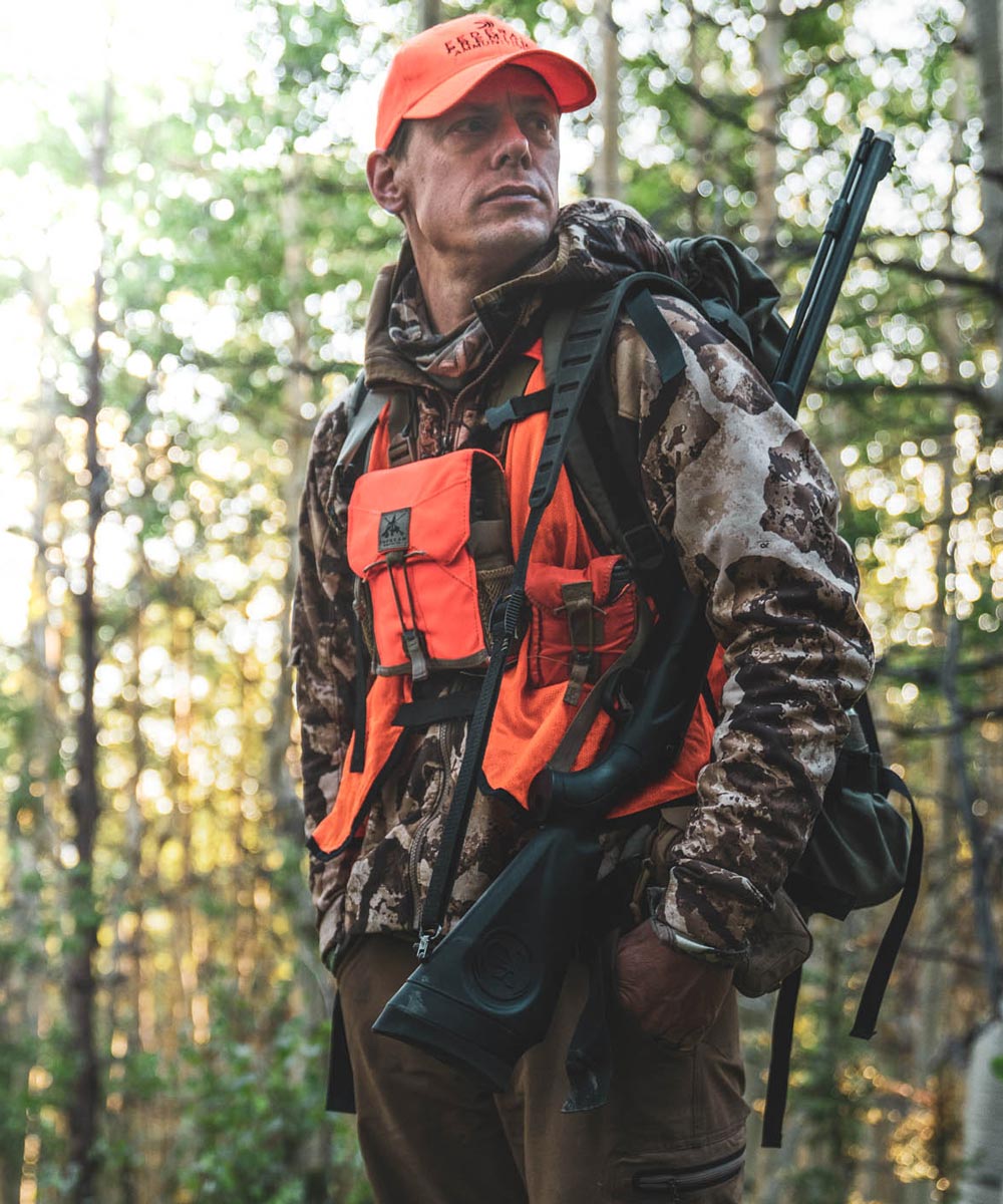 Orange chest hunting pack with multiple pockets on a hunter in the woods.