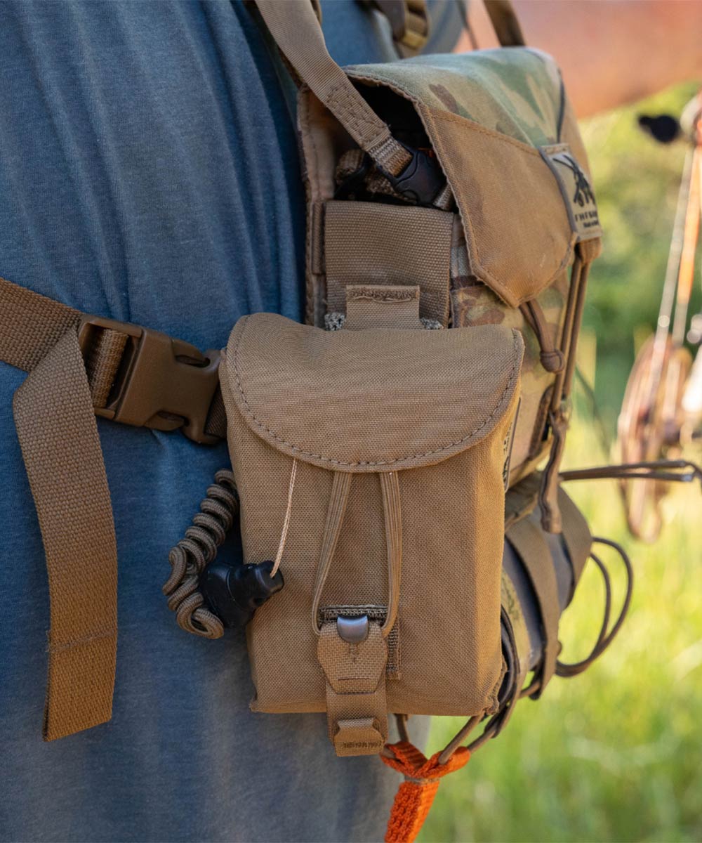 Tan tactical pouch with a flap, front bungee cord, and attached coiled accessory.