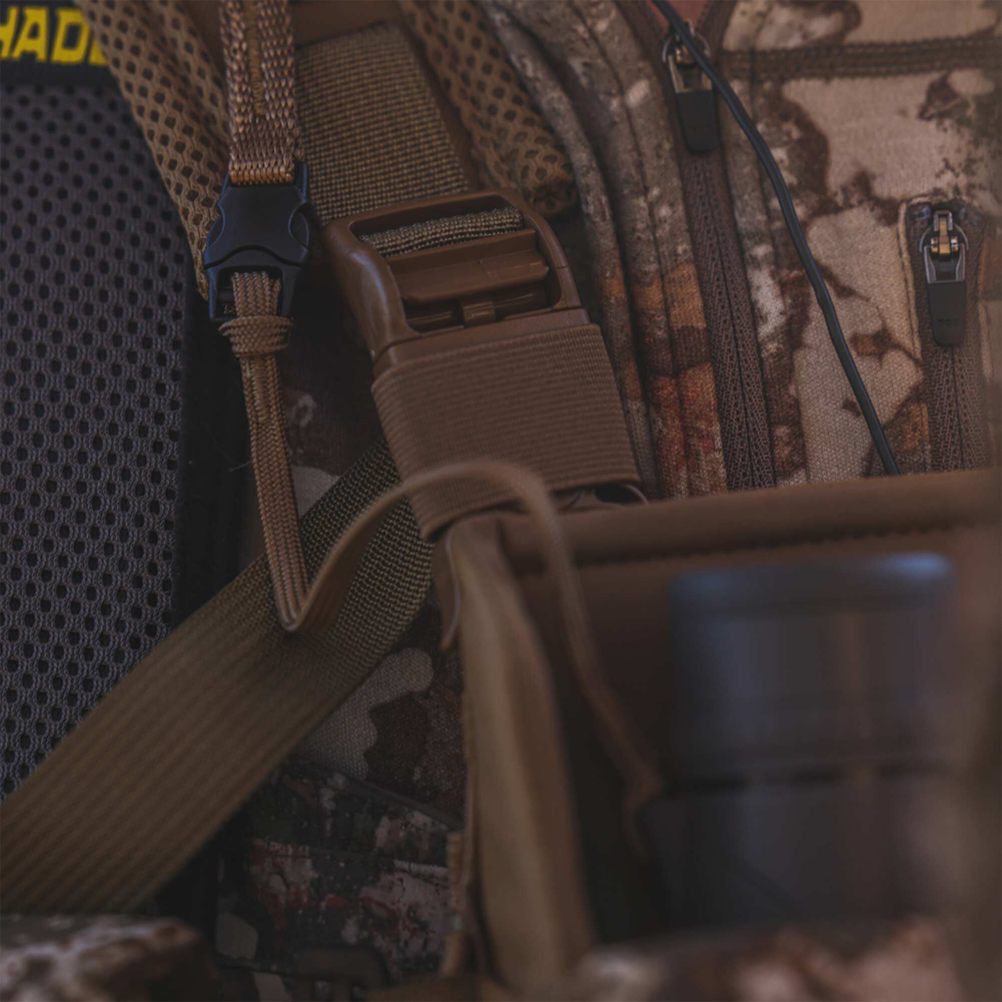 Hades camo hunting backpack with tan straps, black buckles, mesh padding, and zippers.