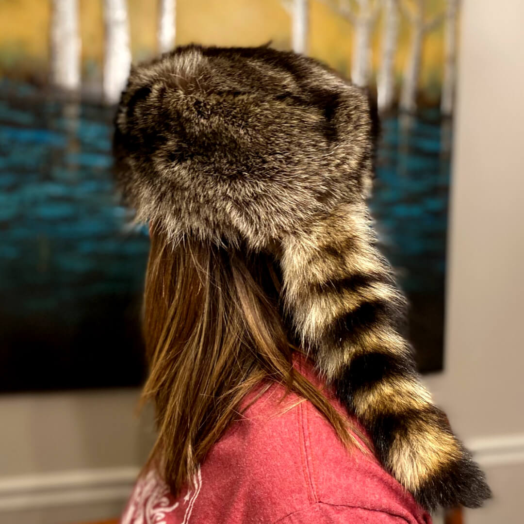 Brown-black raccoon fur hat featuring a long, prominently striped tail.
