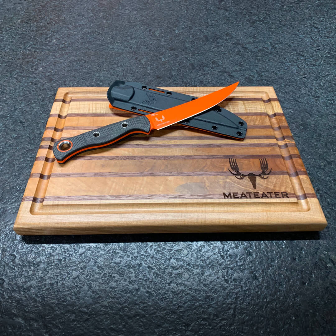 Orange blade fillet knife with black & orange handle and black sheath on wood board.