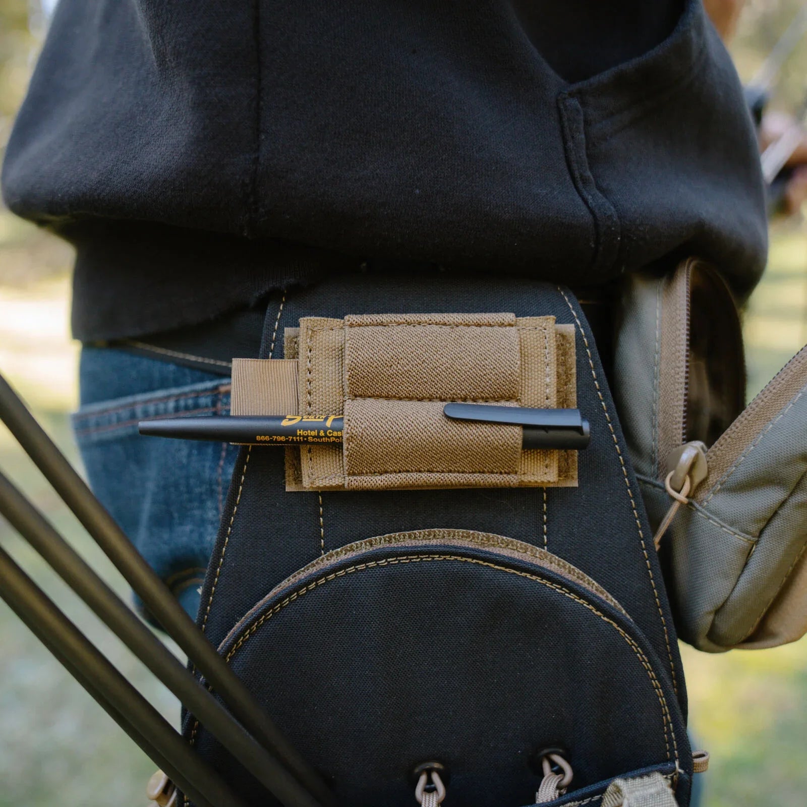Black archery quiver with tan pen holder holding a black pen and several dark arrows.