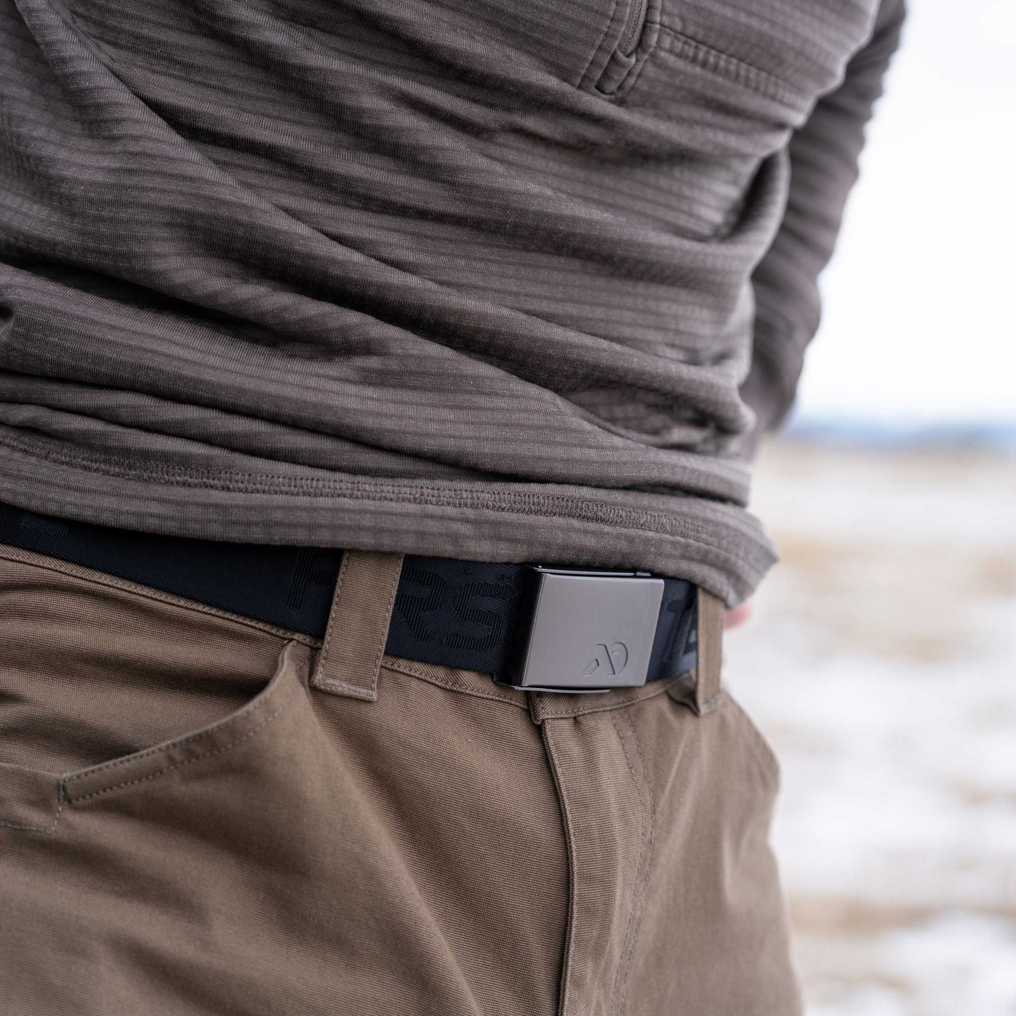 Person wearing a brown sweater and beige pants with a belt, standing outdoors.