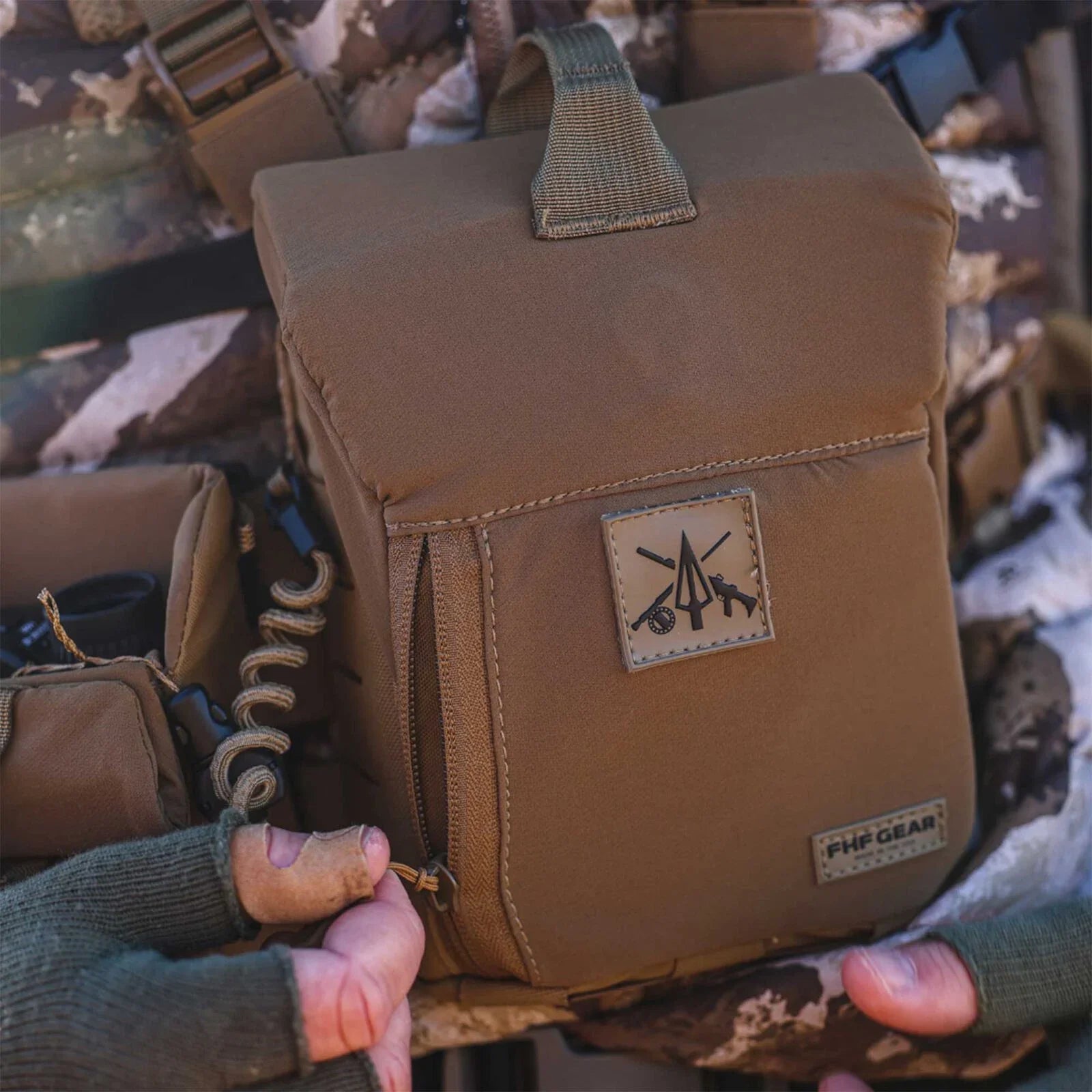 Tan FHF GEAR chest pack with zippered pocket and logo patch, opened by a gloved hand.