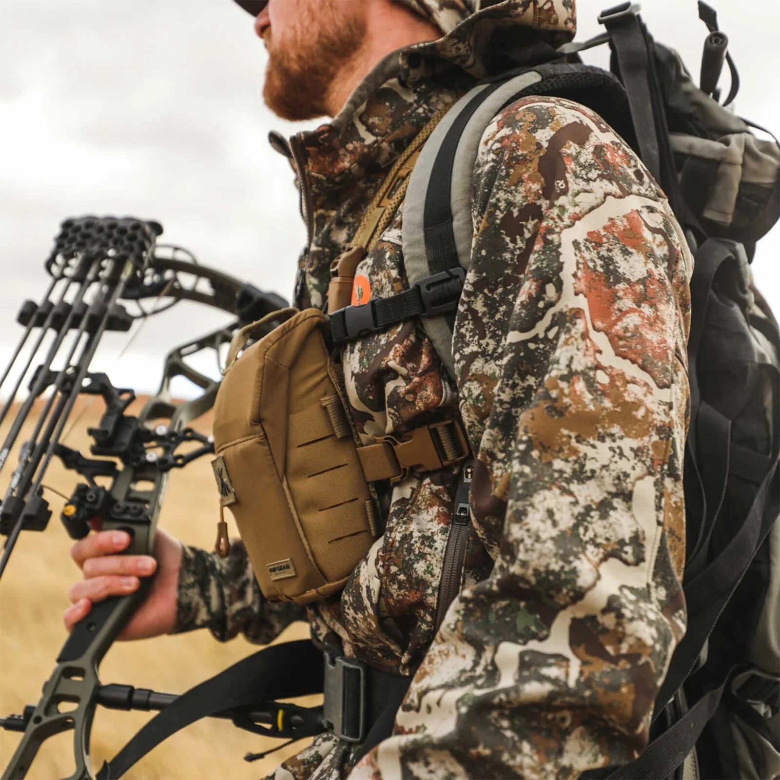 Tan chest pouch with laser-cut slots, worn by a hunter holding a bow.