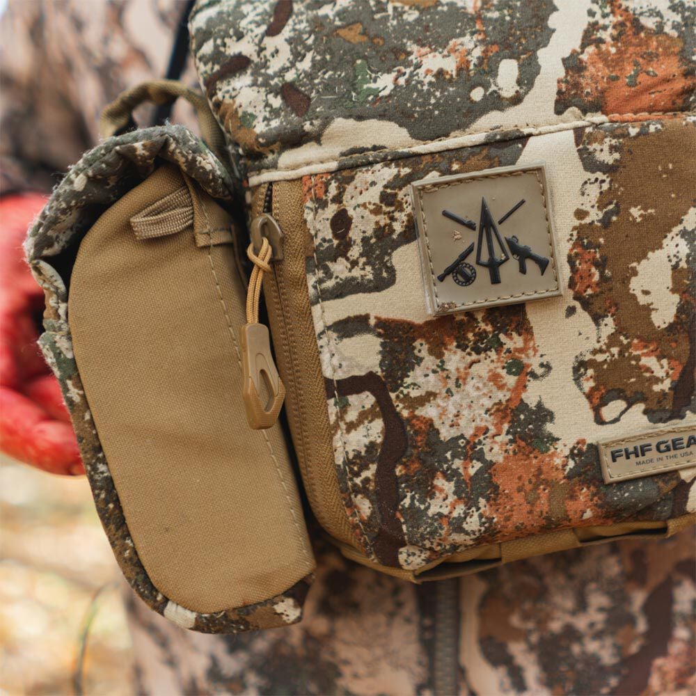 Camo FHF GEAR binocular harness with tan side pouch and hunting emblem patch.