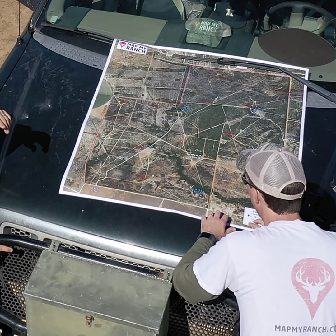 Person views large aerial "Map My Ranch" map on dark vehicle hood.