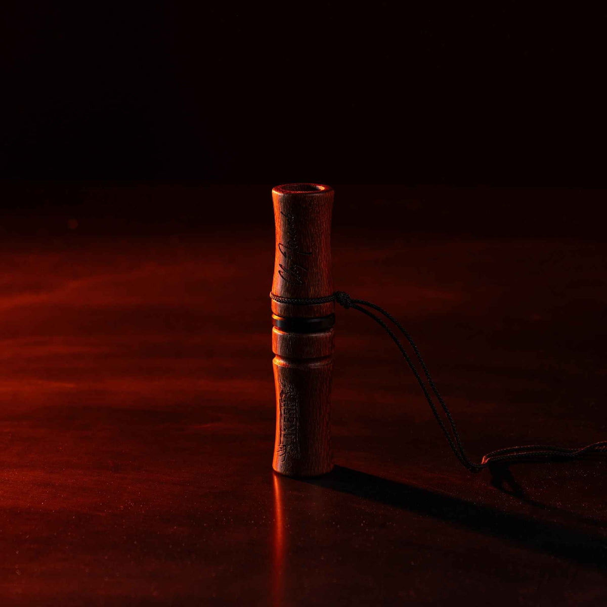 Akern MeatEater x Phelps deer call in a dark room facing red light, it has a cord tied to the middle of it.