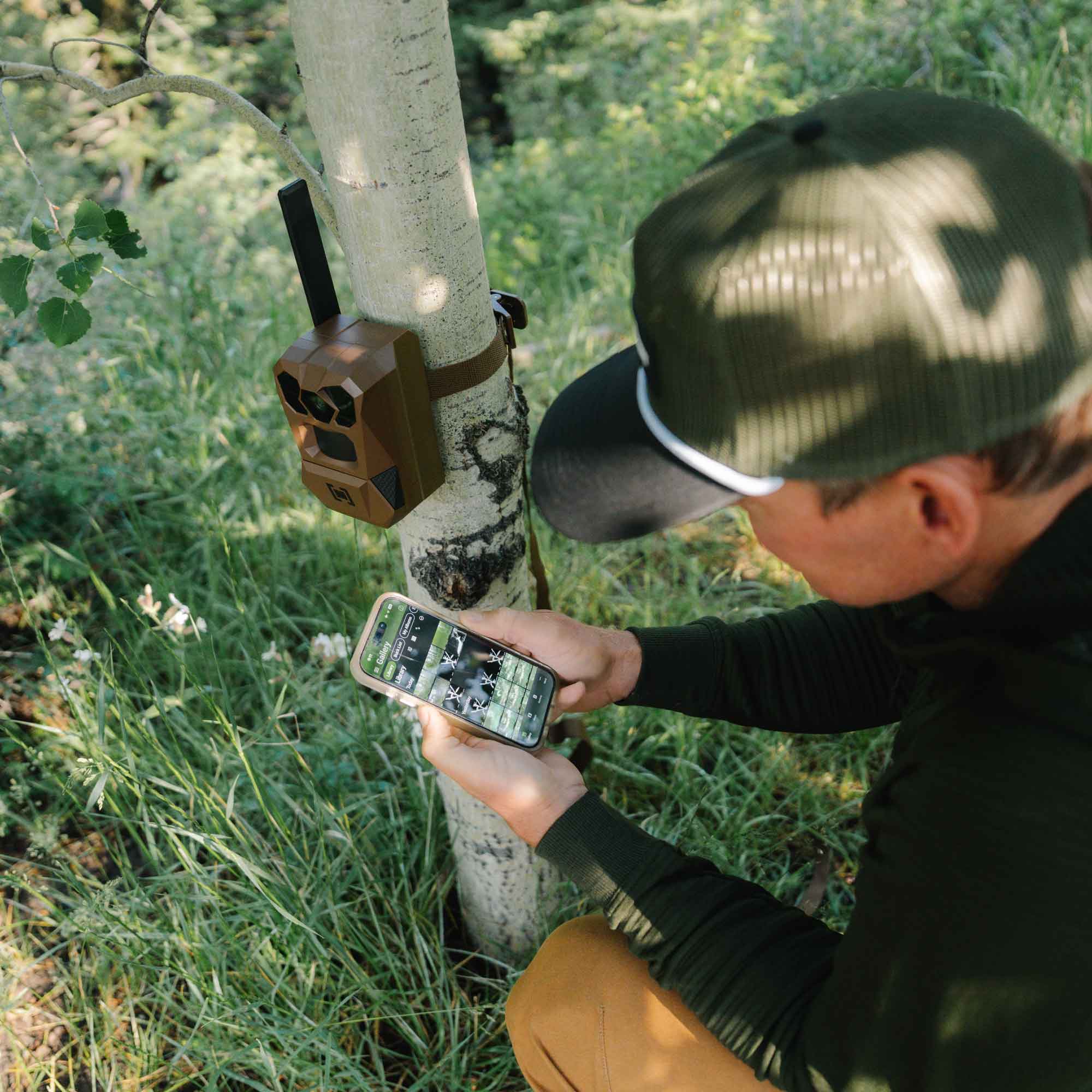 Man with a trail camera connecting it to an app on his phone.