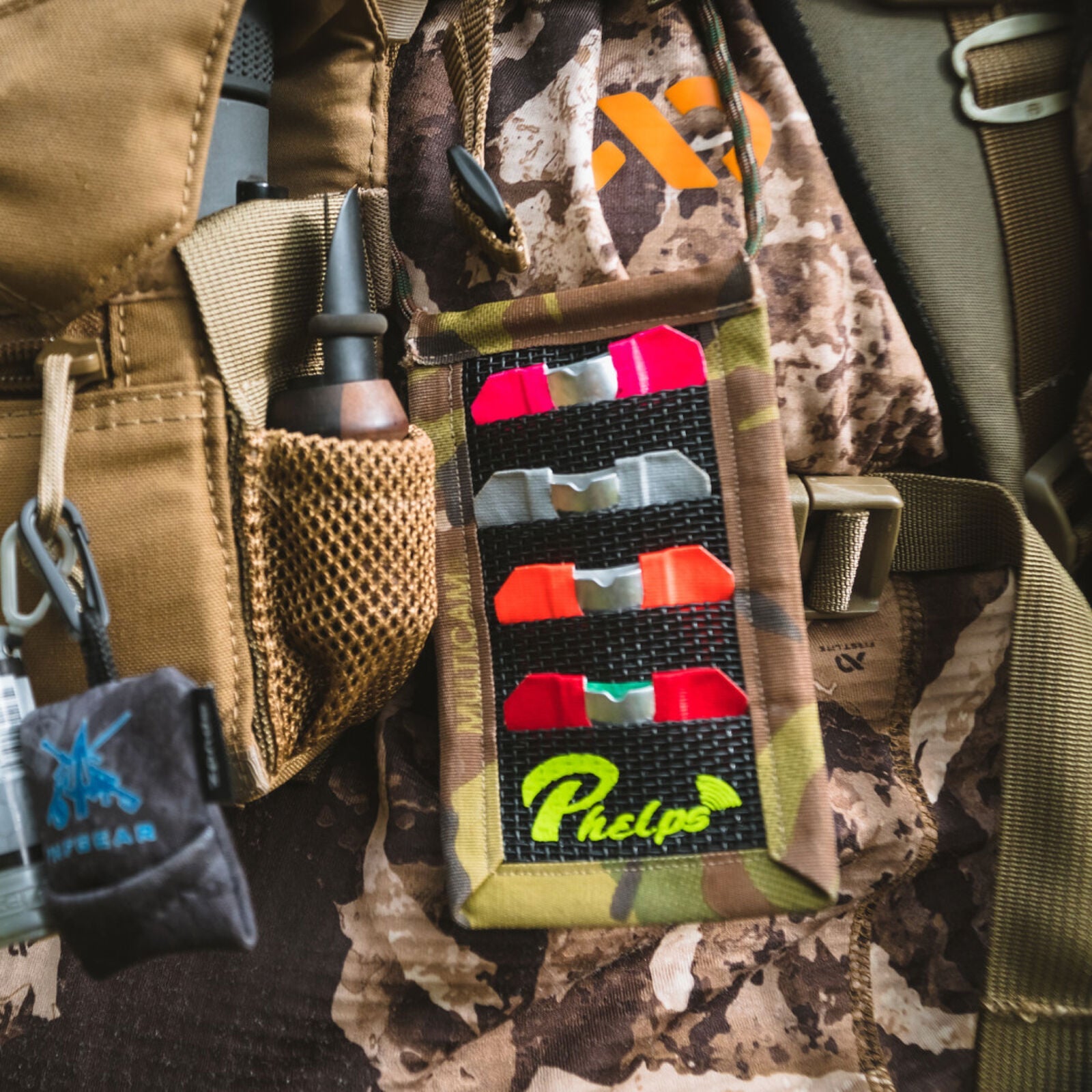 Camouflage hunting vest with Phelps call holder, containing pink, gray, orange, red diaphragm calls.