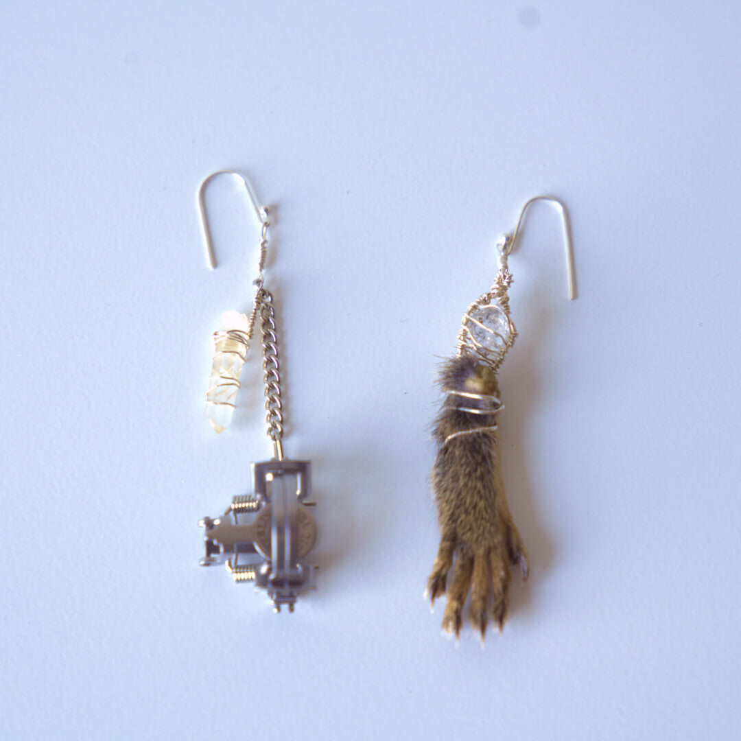 Mismatched earrings: silver mousetrap with crystals, furry brown animal paw with crystal.