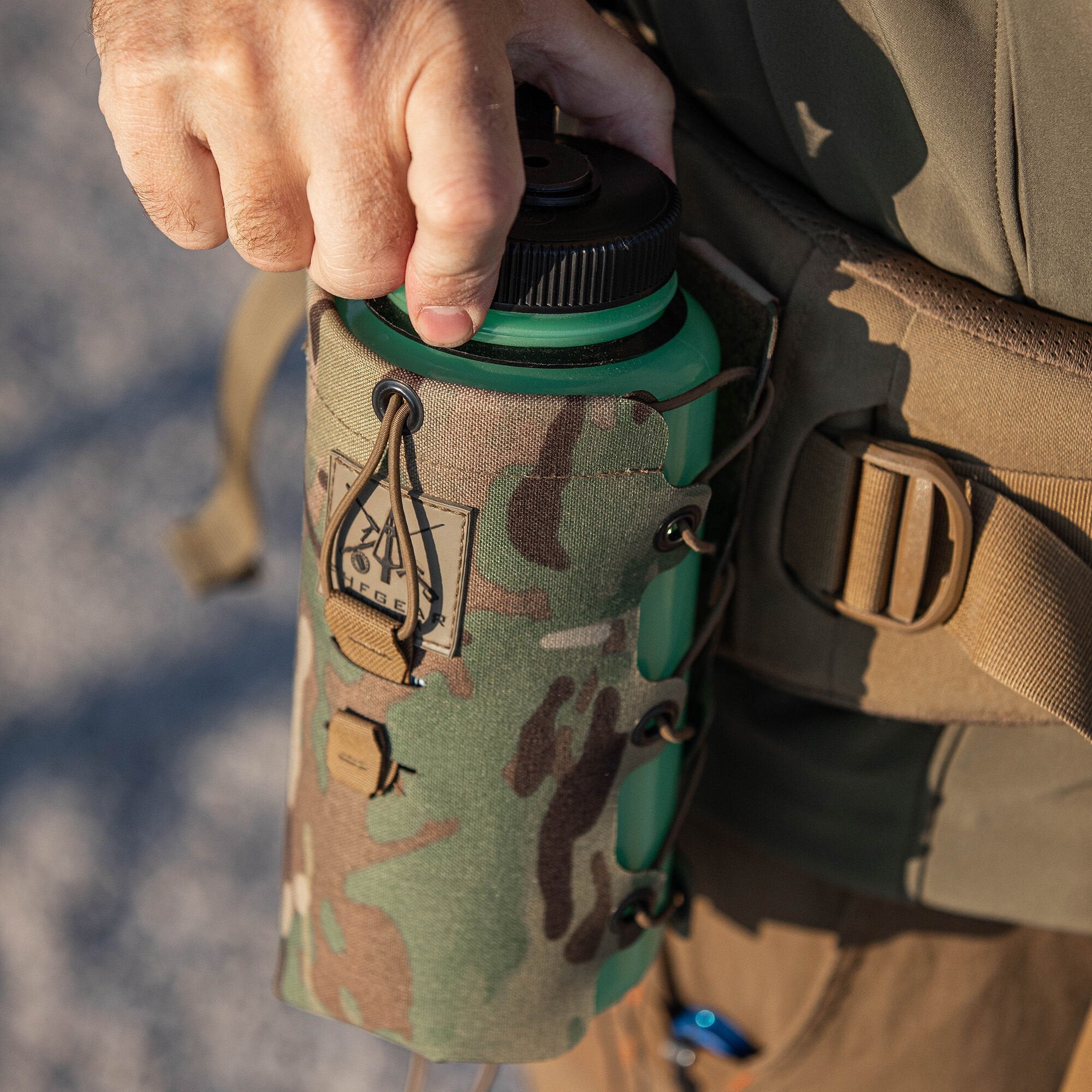 Hand on green water bottle in Multicam pouch with bungee cord lacing.