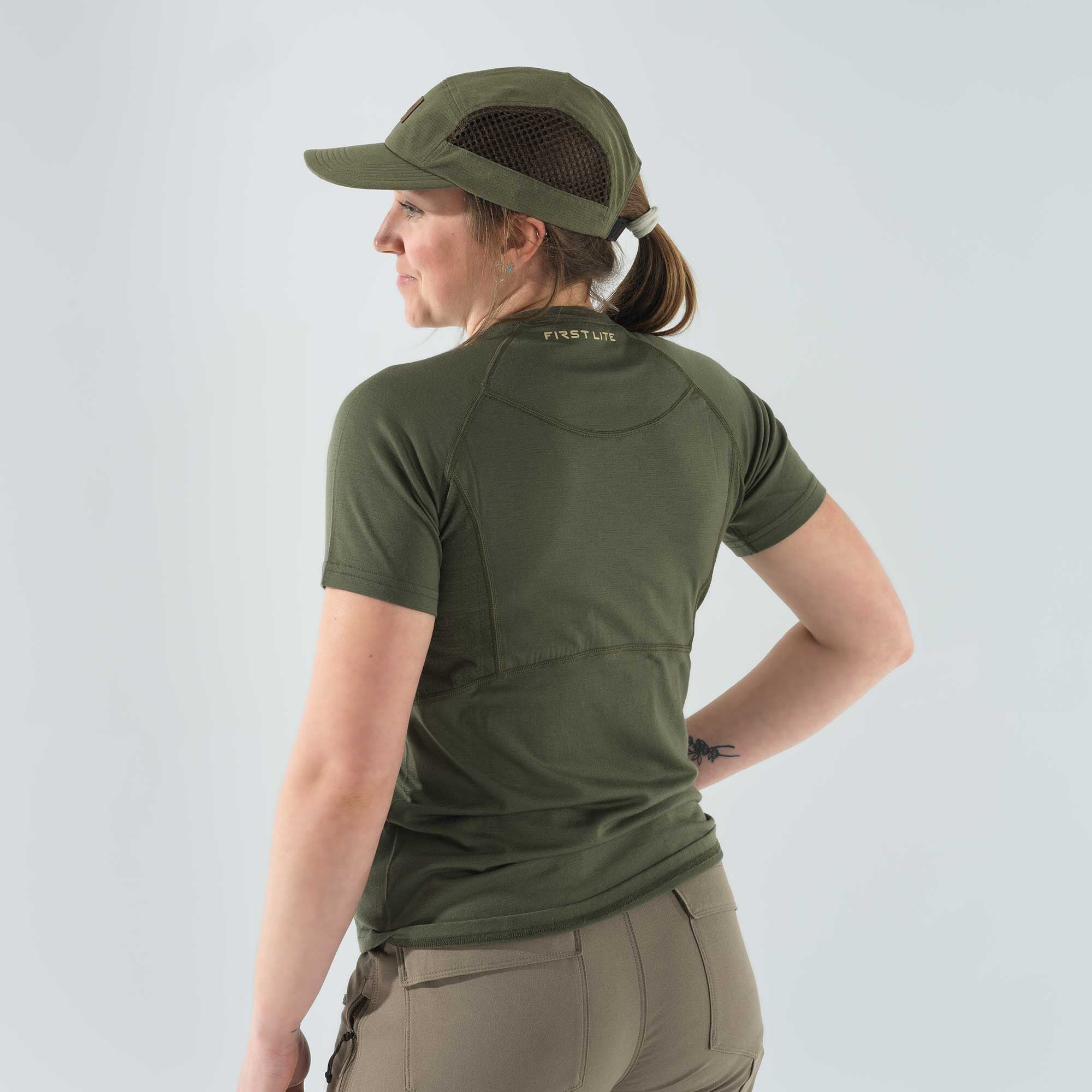 A woman wears an olive green First Lite short-sleeved t-shirt with raglan sleeves and a matching cap featuring mesh side panels.