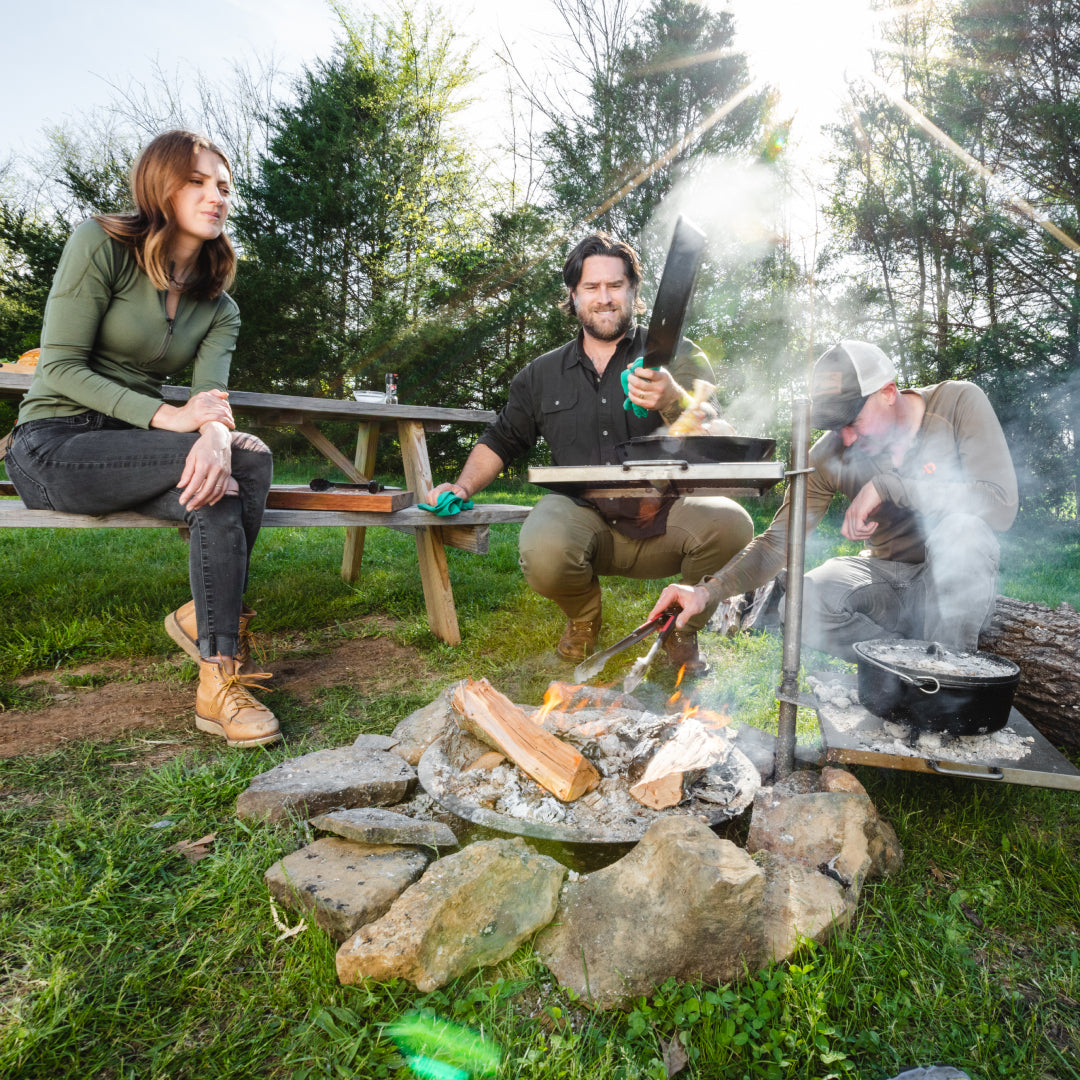 Black outdoor fire pit cooking system with cast iron skillet & Dutch oven over fire.
